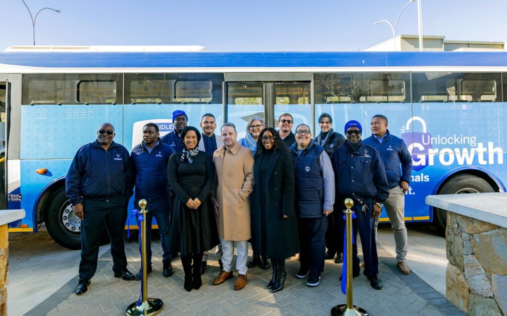 WhatsApp Image 2026-07-04 at 92543 PM - The Brief | Namibia's Leading Business & Financial News Group of professionals posing in front of a blue bus with 'Unlocking Growth' text, outdoors on a sunny day.
