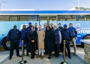 Group of professionals posing in front of a blue bus with 'Unlocking Growth' text, outdoors on a sunny day.