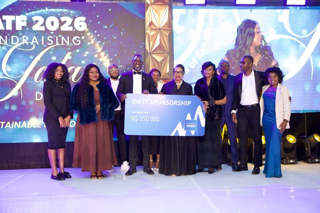 WhatsApp Image 2026-07-05 at 63336 PM - The Brief | Namibia's Leading Business & Financial News Group of ten formally dressed people on a stage holding a large blue sponsorship check that reads 'OATF Sponsorship' for N0,000, with a bright event backdrop on screens behind them.