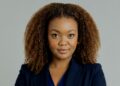 Des-Rose Engelbrecht1 - The Brief | Namibia's Leading Business & Financial News Portrait of a woman with curly hair in a navy blazer, looking at the camera and smiling.