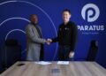 Two men shake hands across a conference table in front of a blue wall with the Paratus logo, signifying a business agreement.
