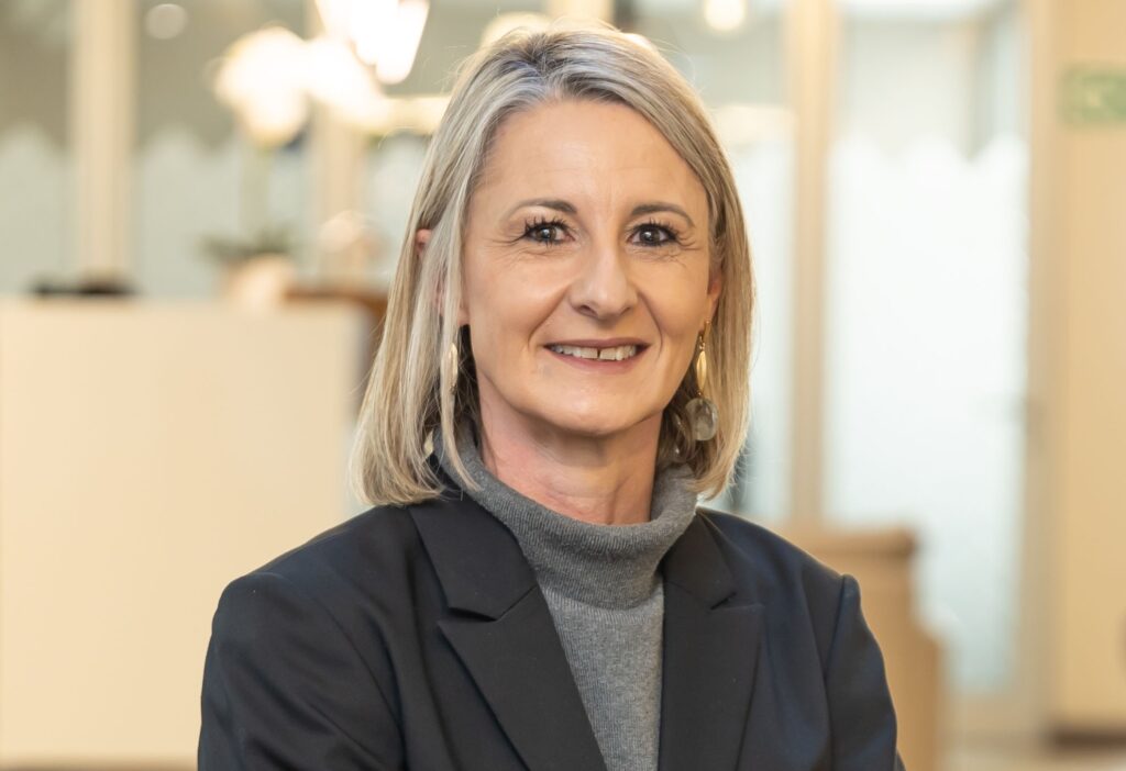 Lorelle Viljoen - The Brief | Namibia's Leading Business & Financial News Portrait of a smiling blonde woman in a gray turtleneck and dark blazer, in an office setting behind her.