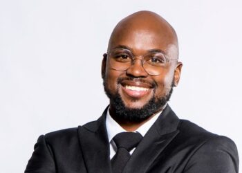 Smiling professional portrait: a man in a black suit and tie with round glasses, facing the camera.