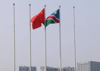China and Namibia national flags flying on flagpoles above a city skyline in the background.