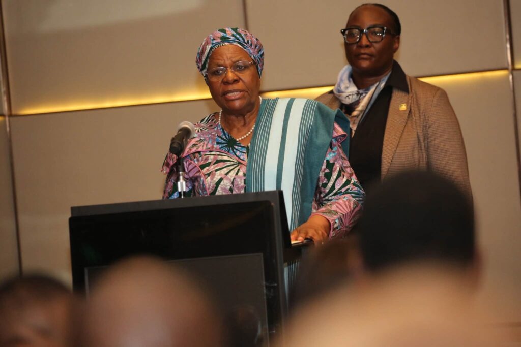 WhatsApp Image 2026-07-09 at 32839 PM - The Brief | Namibia's Leading Business & Financial News Older woman wearing a colorful headwrap and traditional attire speaks at a podium with a microphone, while another woman stands behind her in a blazer.