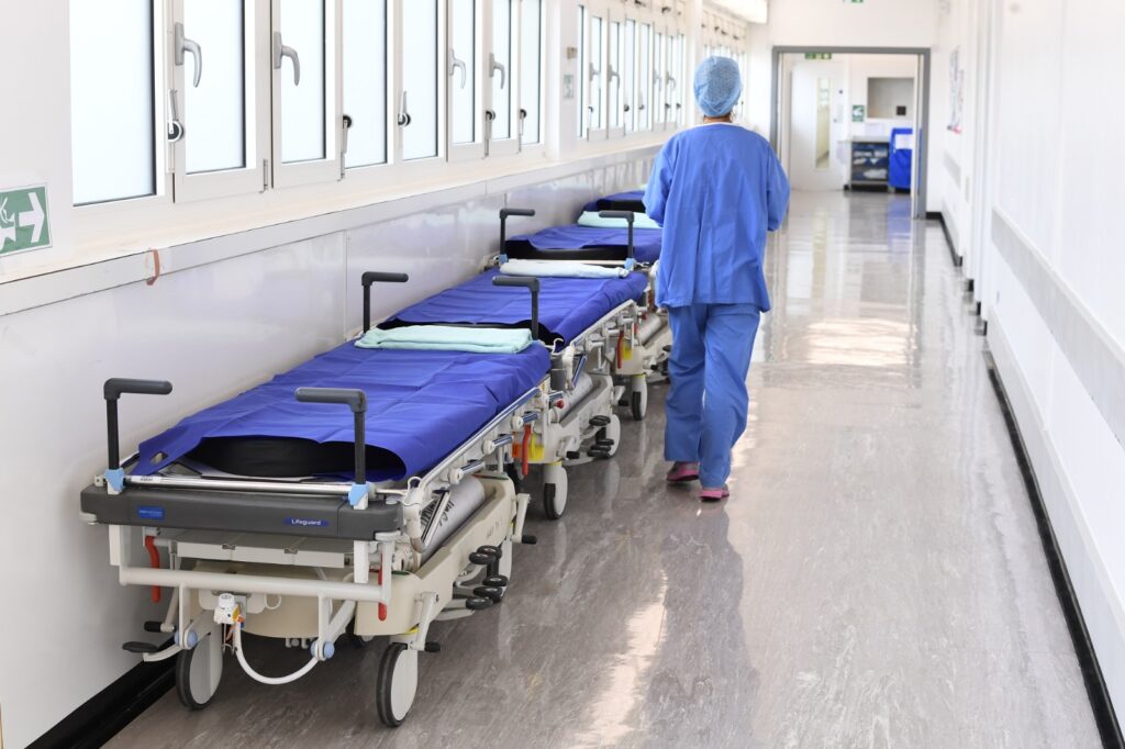 windhoek hospital - The Brief | Namibia's Leading Business & Financial News Hospital hallway with a row of patient stretchers covered in blue sheets along the left wall; a medical professional in blue scrubs walks away down the corridor