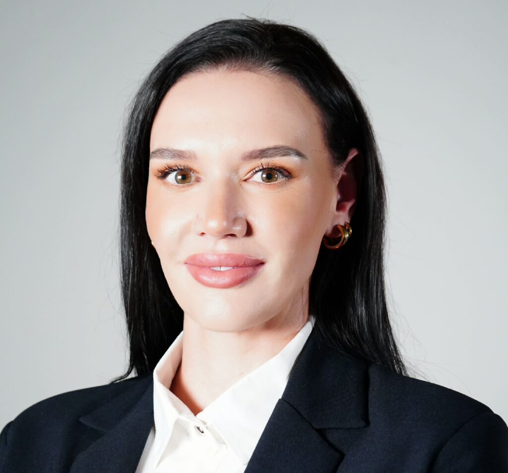 Close-up of a woman in a black blazer and white blouse, showing the upper part of her face and clothing accessory.