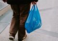 PLASTIC - The Brief | Namibia's Leading Business & Financial News Person walking on an urban sidewalk, holding a bright blue plastic shopping bag.