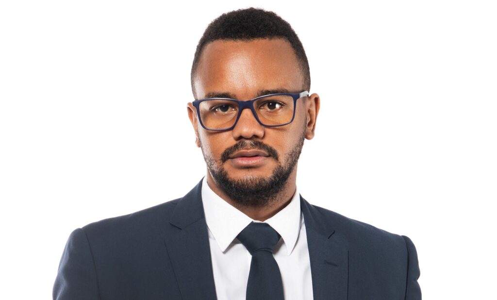 Head-and-shoulders portrait of a man in a navy suit, white shirt, and blue-framed glasses looking at the camera