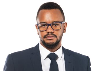 Head-and-shoulders portrait of a man in a navy suit, white shirt, and blue-framed glasses looking at the camera