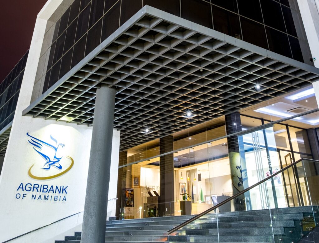 Exterior view of Agribank Namibia storefront with glass doors and blue logo on white wall under a grid-pattern overhang