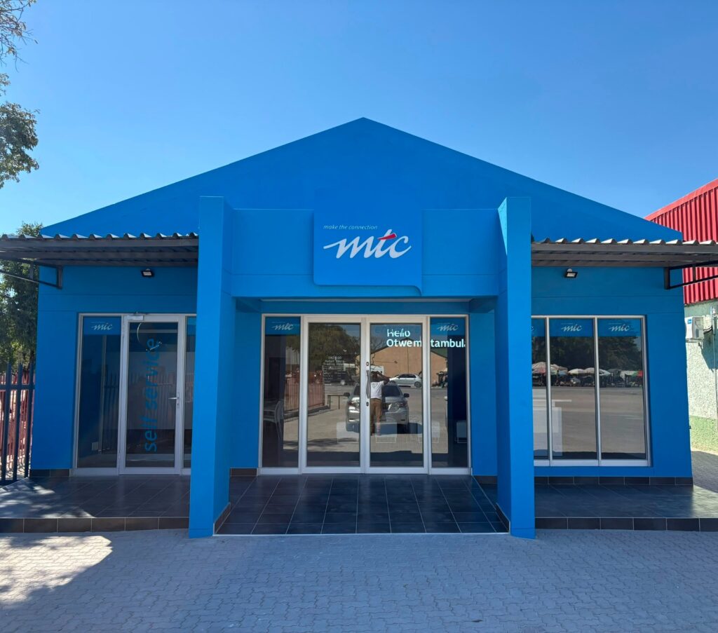 Blue MT C storefront with a peaked roof, glass doors, and 'make the connection' logo above the entrance.