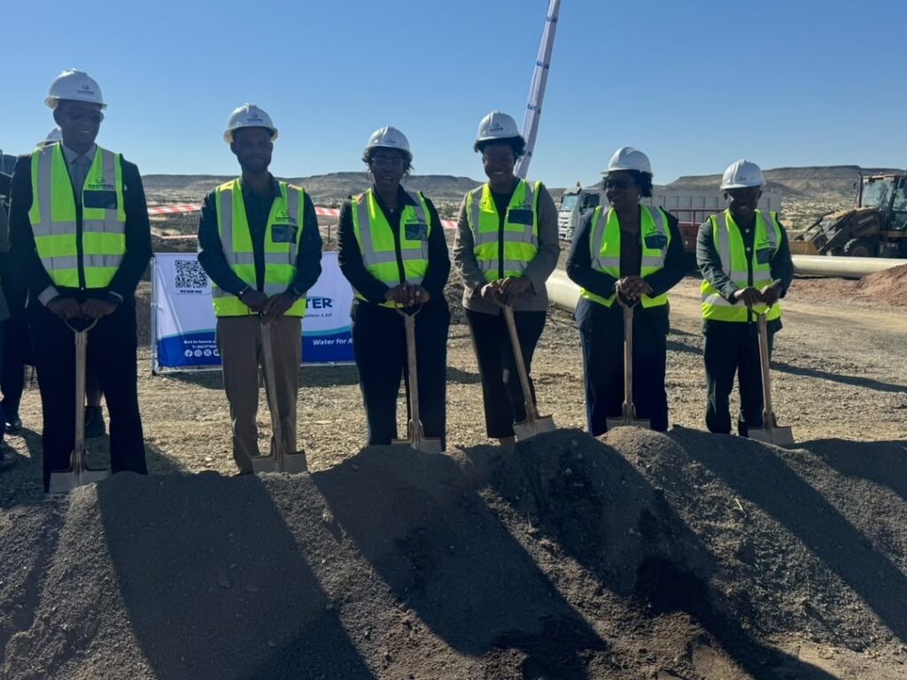 WhatsApp Image 2026-07-16 at 33528 PM - The Brief | Namibia's Leading Business & Financial News Six construction workers wearing hard hats and neon vests stand with shovels in front of a dirt mound at a groundbreaking event on an arid construction site.