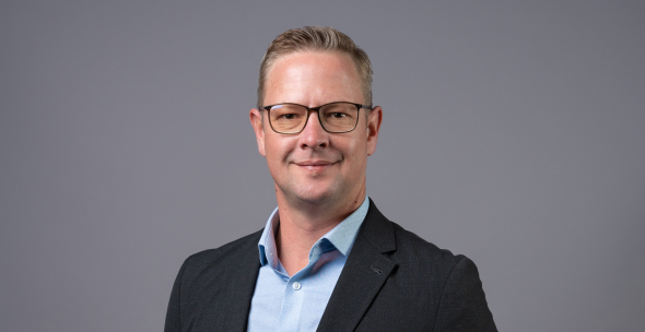 Wynand Oosthuizen - The Brief | Namibia's Leading Business & Financial News Professional headshot: man in a dark blazer and light blue shirt, smiling at the camera against a gray backdrop.