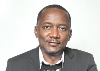 Head-and-shoulders portrait of a man in a dark suit and white shirt, facing the camera with a neutral expression against a light background.