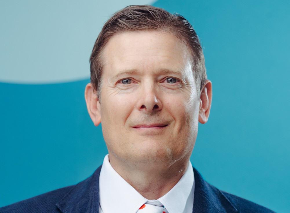 Frederick Muller - The Brief | Namibia's Leading Business & Financial News Head-and-shoulders portrait of a smiling man in a navy suit and white shirt against a teal background.