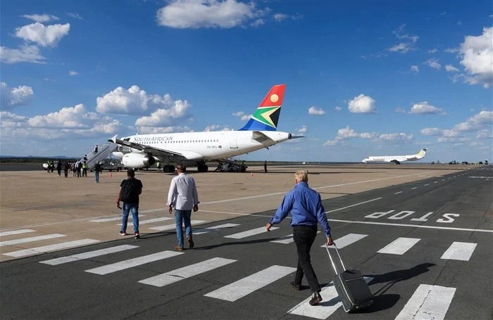 Passengers1 - The Brief | Namibia's Leading Business & Financial News Passengers walk on the tarmac toward a South African Airways plane parked at a gate, under a blue sky with white clouds.