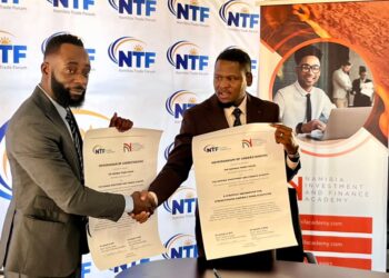 Two suited men shake hands and display signed memorandum papers at a Namibia Trade Forum backdrop.