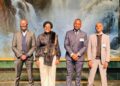WhatsApp Image 2026-07-21 at 43514 PM - The Brief | Namibia's Leading Business & Financial News Four professionally dressed individuals pose together for a group photo in front of a waterfall backdrop, smiling at the camera in a formal setting.
