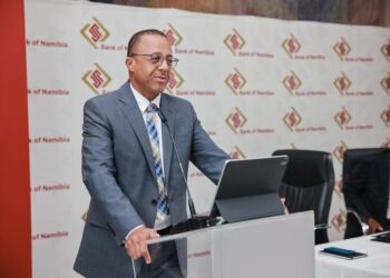 Man in a gray suit delivers a speech at a podium, with a Bank of Namibia backdrop behind him.