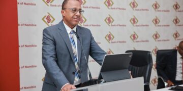 Man in a gray suit delivers a speech at a podium, with a Bank of Namibia backdrop behind him.