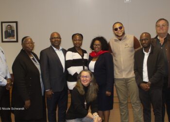 Group of ten adults posing for a photo in a meeting room, one woman kneeling in front and the rest standing, all smiling.