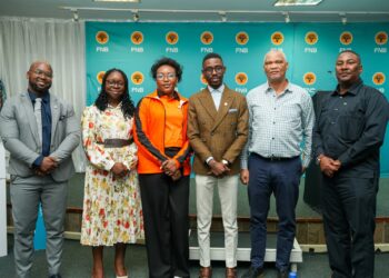 Group of six professionals posing for a photo at a corporate event, standing in front of a blue FNB backdrop.