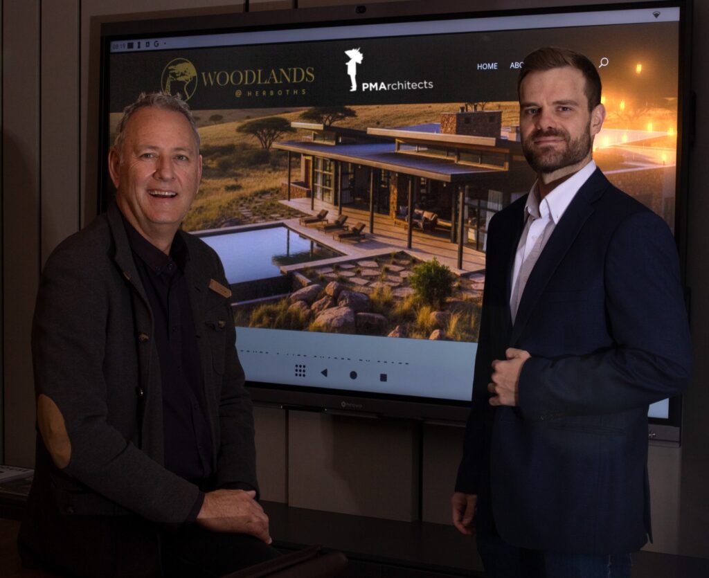 WhatsApp Image 2026-07-27 at 43526 PM - The Brief | Namibia's Leading Business & Financial News Two men stand beside a large screen showing a modern house rendering with Woodlands branding in a showroom setting.