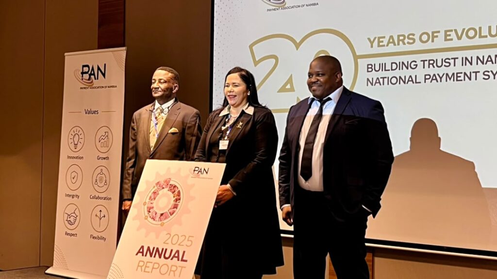 WhatsApp Image 2026-07-28 at 35110 PM - The Brief | Namibia's Leading Business & Financial News Three professionals in business attire stand on a stage at a PAN Namibia event, beside an 'Annual Report 2025' sign.