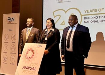 Three professionals in business attire stand on a stage at a PAN Namibia event, beside an 'Annual Report 2025' sign.
