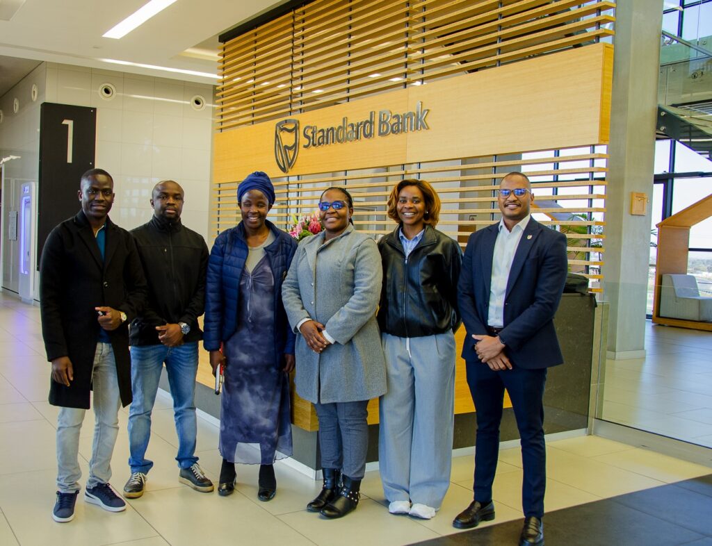 WhatsApp Image 2026-07-28 at 43043 PM - The Brief | Namibia's Leading Business & Financial News Six people stand together and smile in a Standard Bank lobby, posing in front of a wood-slatted wall and bank sign.
