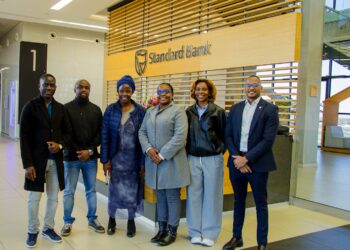 Six people stand together and smile in a Standard Bank lobby, posing in front of a wood-slatted wall and bank sign.