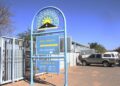 ROADS AUTHORITY - The Brief | Namibia's Leading Business & Financial News Blue metal arch sign for a Road Authority drive-through vehicle license renewal, with a parked SUV and a person in the background near the building.