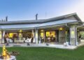 WhatsApp Image 2026-07-29 at 50625 PM - The Brief | Namibia's Leading Business & Financial News Outdoor patio with white seating, a fire pit on the lawn, and a modern house with large glass doors open to an interior seating area at dusk.