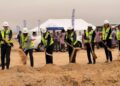 WhatsApp Image 2026-07-30 at 102731 AM - The Brief | Namibia's Leading Business & Financial News Group of professionals in hard hats and high-visibility vests dig with shovels at a desert groundbreaking ceremony, with a white tent and onlookers in the background.