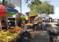 Outdoor street market with colorful umbrellas and fruit stalls along a sunny sidewalk.