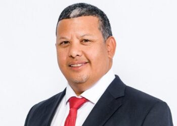 Professional headshot of a man in a dark suit and red tie against a white background.