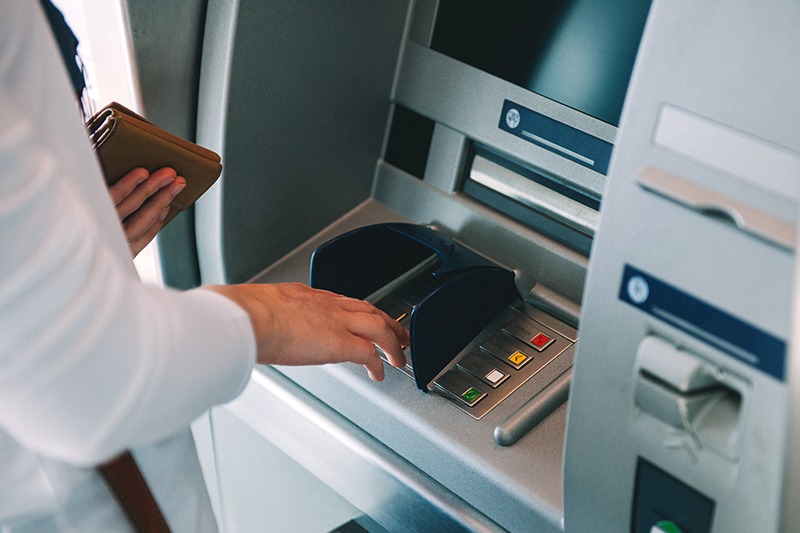 ATM1 - The Brief | Namibia's Leading Business & Financial News Person using an ATM, inserting a card while holding a wallet nearby in a bank lobby