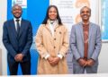Three professionally dressed individuals stand side by side smiling in front of banners for the Economic Association of Namibia (Namibia business event).