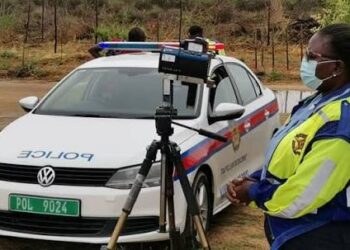 traffic officer - The Brief | Namibia's Leading Business & Financial News Female police officer in a neon jacket and mask stands beside a white patrol car with a camera on a tripod for speed enforcement.