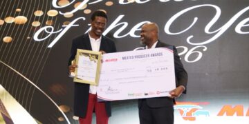 Two men in suits on a stage, smiling as one presents a framed certificate and a large ceremonial check at an awards event with a decorative backdrop.