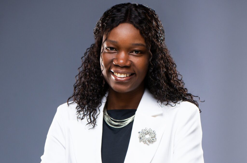 Priscila Chilombo1 - The Brief | Namibia's Leading Business & Financial News Professional portrait of a smiling Black woman wearing a white blazer, black top, silver necklace, and brooch against a gray backdrop.