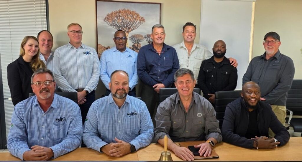 WhatsApp Image 2026-08-04 at 105818 AM - The Brief | Namibia's Leading Business & Financial News Twelve professionals posing for a group photo in a modern conference room, seated and standing around a wooden table with artwork on the wall behind them.
