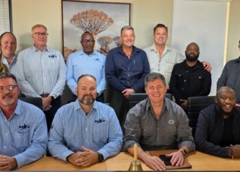 Twelve professionals posing for a group photo in a modern conference room, seated and standing around a wooden table with artwork on the wall behind them.