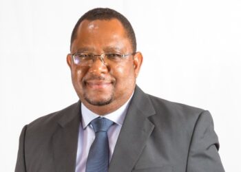 Professional portrait of a smiling man in a dark suit and blue tie against a white background with glasses on.