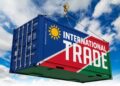 Blue shipping container being lifted by a crane, painted with a bold 'INTERNATIONAL TRADE' banner and sun emblem against a blue sky.