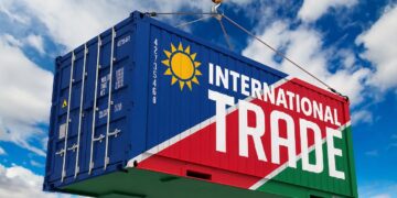 Blue shipping container being lifted by a crane, painted with a bold 'INTERNATIONAL TRADE' banner and sun emblem against a blue sky.