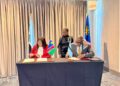WhatsApp Image 2026-08-07 at 115335 AM - The Brief | Namibia's Leading Business & Financial News Two officials sign documents at a table with small flags (Namibia and Botswana) as a colleague looks on in a formal signing ceremony behind tall curtains and national flags.