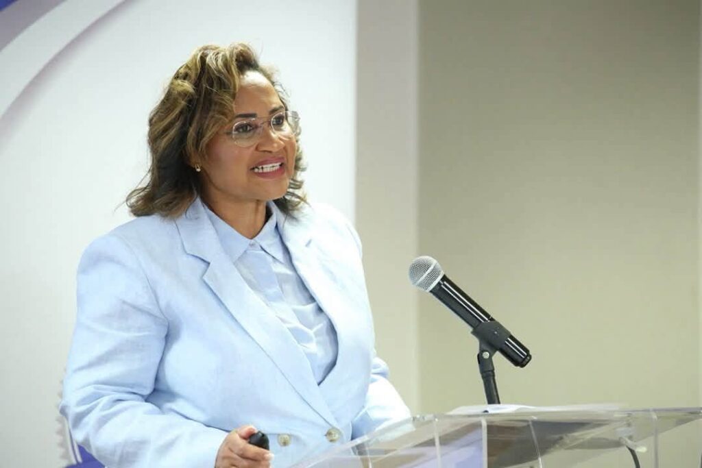 Patty Karuaihe-Martin2 - The Brief | Namibia's Leading Business & Financial News Woman in a light blue blazer speaks at a clear acrylic podium with a microphone, smiling as she presents.
