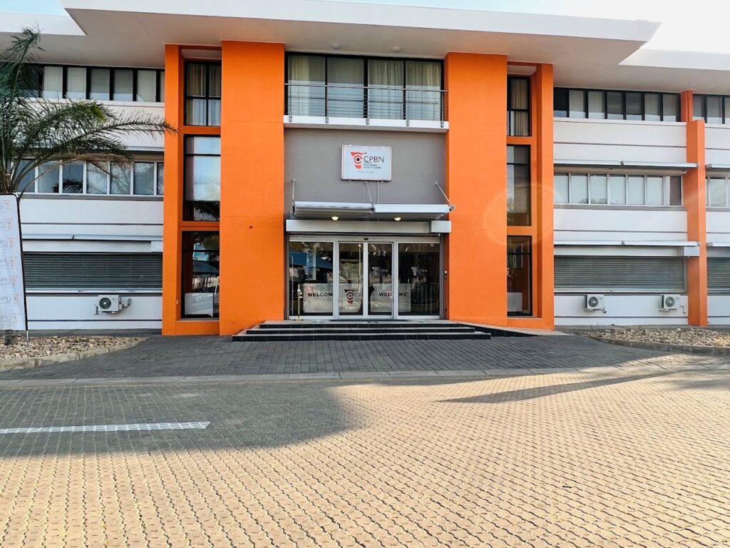 Front entrance of a modern white building with bright orange vertical columns, glass doors, and a small CPBN sign above the doorway.